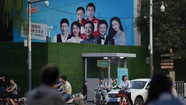 People wait to cross a road below security cameras and in front of a newly-installed guard post outside the Worker's Stadium in Beijing, where karaoke bars are closing, toy bombs are banned and every delivery package is being scanned as authorities are taking no chances weeks ahead of a massive military parade to mark Communist China's 70th anniversary, Oct. 1, 2019.