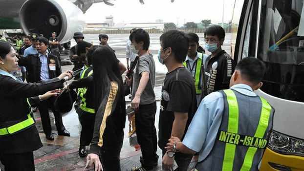 This handout photo shows security personnel in Manila checking illegal immigrants from Taiwan and China, accused of running a multi-million dollar online and phone scam, before they were deported by Philippine authorities, Sept.19, 2012.