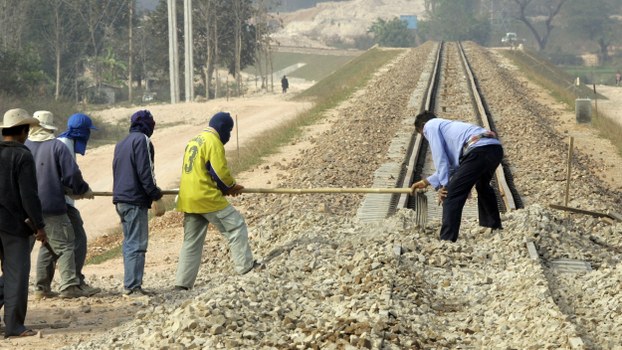 In a file photo, construction workers rake gravel  on the new railroad tracks across the Thai_Lao Friendship bridge in Thanalaeng, Laos. 