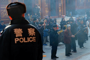 A Chinese policeman looks on as Buddhist worshippers (R) make wishes at the Tibetan Lama Temple in Beijing, Jan. 25, 2012.
